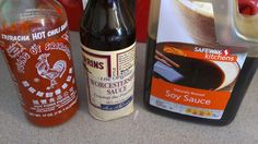 two bottles of hot sauce next to each other on a counter with an empty container