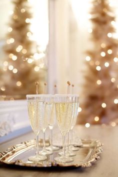 three glasses of champagne sitting on a tray in front of a christmas tree