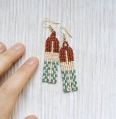 a pair of beaded earrings is being held up by someone's hand on a white surface