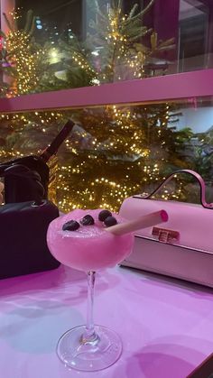 a pink cocktail sitting on top of a table next to a handbag and purse