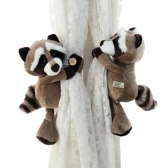 two stuffed raccoons are hanging on the curtains in front of a white lace curtain