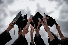 a group of people in graduation caps and gowns holding their hands up to the sky