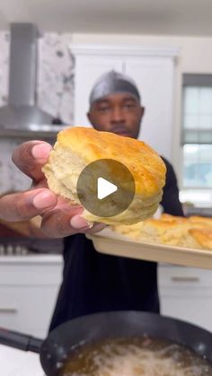 a man holding up a piece of bread in his hand while standing next to a frying pan filled with food