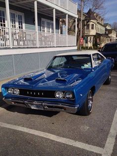 a blue muscle car parked in front of a building with white balconies on it