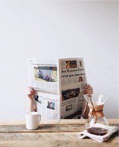 a person sitting at a table reading a newspaper with a cup of coffee in front of them