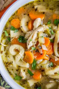 a white bowl filled with chicken noodle soup on top of a wooden table next to an orange napkin