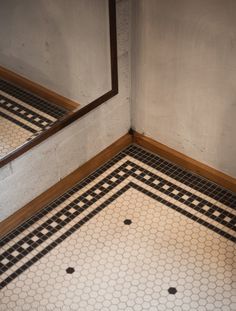 the corner of a bathroom with black and white tile on the floor next to a mirror