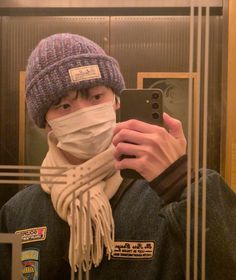 a man wearing a hat and scarf taking a selfie in front of a mirror