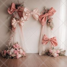 three bows are hanging on the wall in front of two windows with pink flowers and greenery