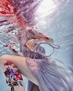 a woman with long purple hair is under the water and has her arms wrapped around her body