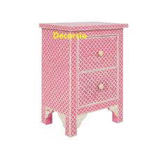 a pink and white dresser with two drawers on one side, and an ornate pattern on the other