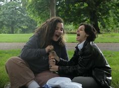 two women sitting on the ground laughing and holding onto each other's hands in a park