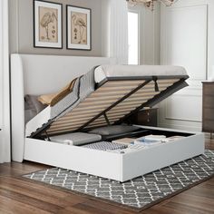 a white bed with an open box underneath it on top of a carpeted floor