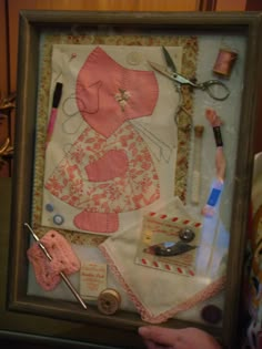 a person holding up a framed artwork with scissors and sewing supplies