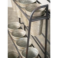 several buckets are stacked up on a metal rack with black handles and two rows of silver cups