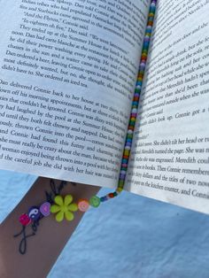 a person holding an open book with colorful beads on their wrist and the pages are folded in half