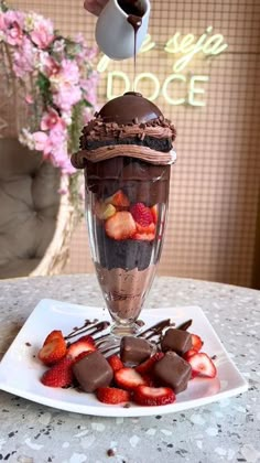 a chocolate dessert with strawberries and ice cream on a white plate next to a pink flower vase