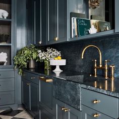 a kitchen with marble counter tops and gold faucets on the sink, surrounded by blue cabinets