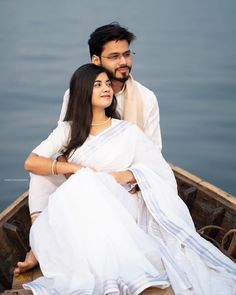 a man and woman sitting in a small boat on the water with their arms around each other