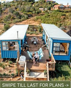 two blue shipping containers sitting on top of a wooden deck next to a lush green hillside