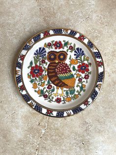 a plate with an owl painted on it sitting on the floor next to a wall