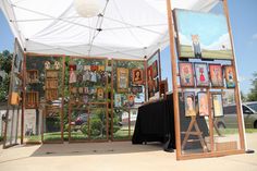 an outdoor art display with paintings and pictures on the walls under a white tent outdoors