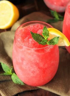 two glasses filled with watermelon lemonade and mint garnish on a brown napkin