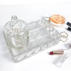 a clear glass container with lipstick, key chain and other items next to it on a white surface