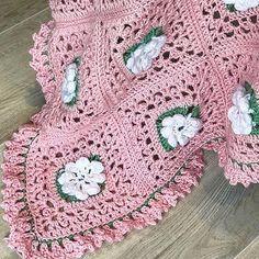 a pink crocheted blanket with white flowers on it sitting on a wooden floor