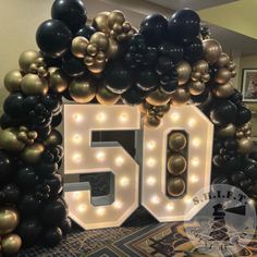 the 50th birthday sign is made out of black, gold and white balloons with lights