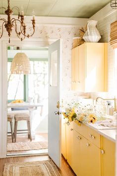 an open door leading to a kitchen with yellow cabinets and flowers on the counter top