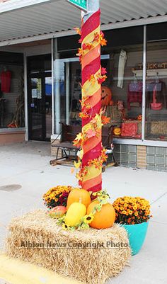 a street sign on top of hay with flowers and pumpkins in front of it