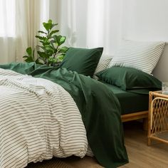 a bed with green sheets and pillows in a white room next to a plant on the floor