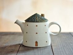 a ceramic tea pot with a small house on the top is sitting on a wooden table