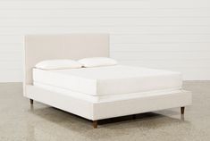 a white bed with two pillows on top of the headboard and foot board, in front of a white wall