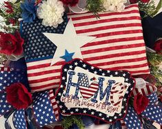 an american flag pillow with the word mom written on it and flowers around it in red, white, and blue colors