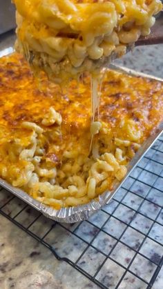 a person is scooping macaroni and cheese out of a pan on a cooling rack