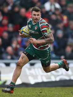 a rugby player runs with the ball in his hand as people watch from the stands