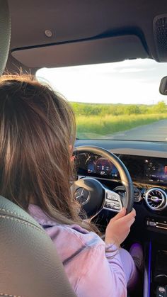 a woman driving a car on a road with grass in the background