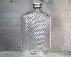 an empty glass bottle sitting on top of a stone table next to a gray wall