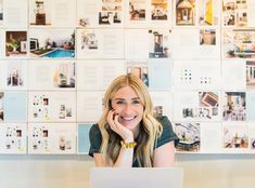 a woman sitting at a table with a laptop computer in front of her and lots of pictures on the wall behind her