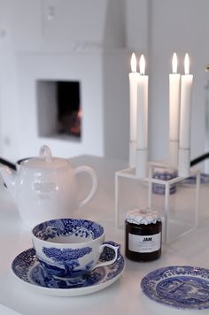 tea cups and saucers on a white table with lit candles in the fireplace behind them