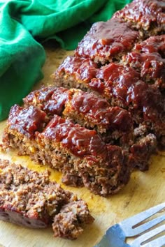 sliced meatloaf sitting on top of a wooden cutting board next to a fork