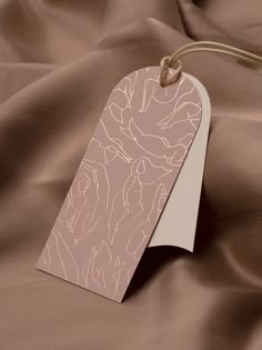 a tag is hanging from a string on a brown satin material with gold foiling