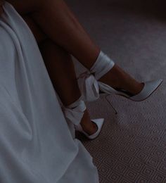 a woman is sitting on the floor wearing high heels and a white dress with straps