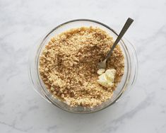 a glass bowl filled with food on top of a white marble countertop next to a metal spoon