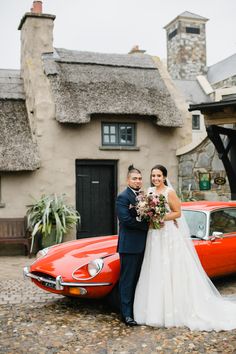 a bride and groom standing in front of an old red sports car at their wedding