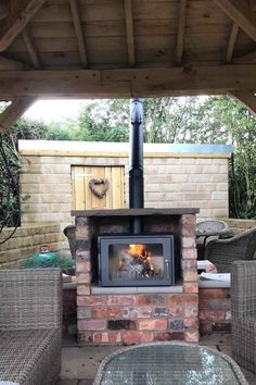 an outdoor fireplace with wicker chairs around it and a table on the patio next to it