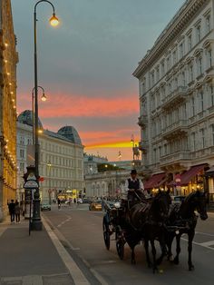 a horse drawn carriage traveling down a street next to tall buildings with lights on them