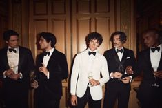 a group of men in tuxedos standing next to each other holding wine glasses